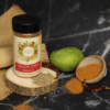 Calcutta Chaat Masala shown in a bottle and a bowl, with raw mango and red chilies placed next to them, emphasizing the spice blend and its natural ingredients