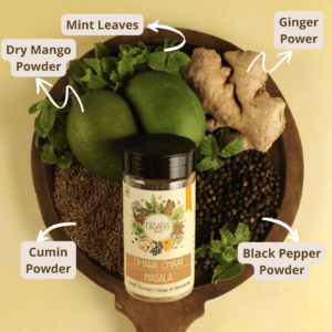 Dhaba Chaat Masala in a bottle, surrounded by raw mango slices, black peppercorns, cumin seeds, dry mango powder, mint leaves, and ginger, showcasing the diverse ingredients of the spice blend
