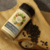 Malabar Kaali Mirch powder in a bottle, with whole black peppercorns scattered beside it, showcasing the ground spice and its raw form