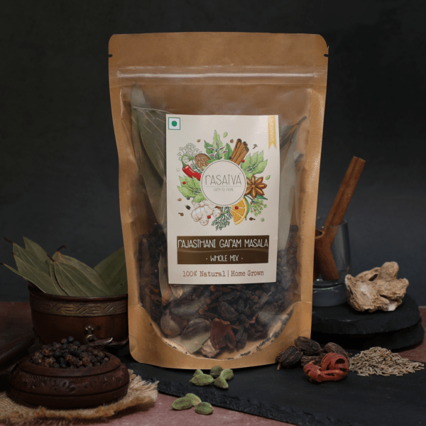 A vibrant mix of whole Rajasthani Garam Masala spices, including cinnamon sticks, cardamom pods, cloves, and peppercorns, arranged on a rustic wooden surface.