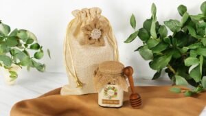 A wooden drizzler rests next to a jar of wild forest honey with a jute bag, highlighting a simple and elegant gifting option