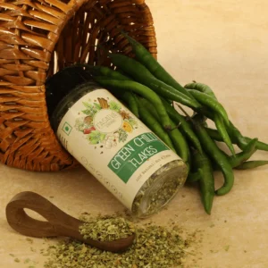 Green chili flakes in a bottle, with a spoon, alongside raw green chilies, showcasing the spice's different presentations and its fresh source.