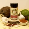 Close-up of Garlic Chutney Masala in a glass bottle and a bowl, with fresh garlic cloves and whole red chilies arranged around, showcasing the spices and their raw forms