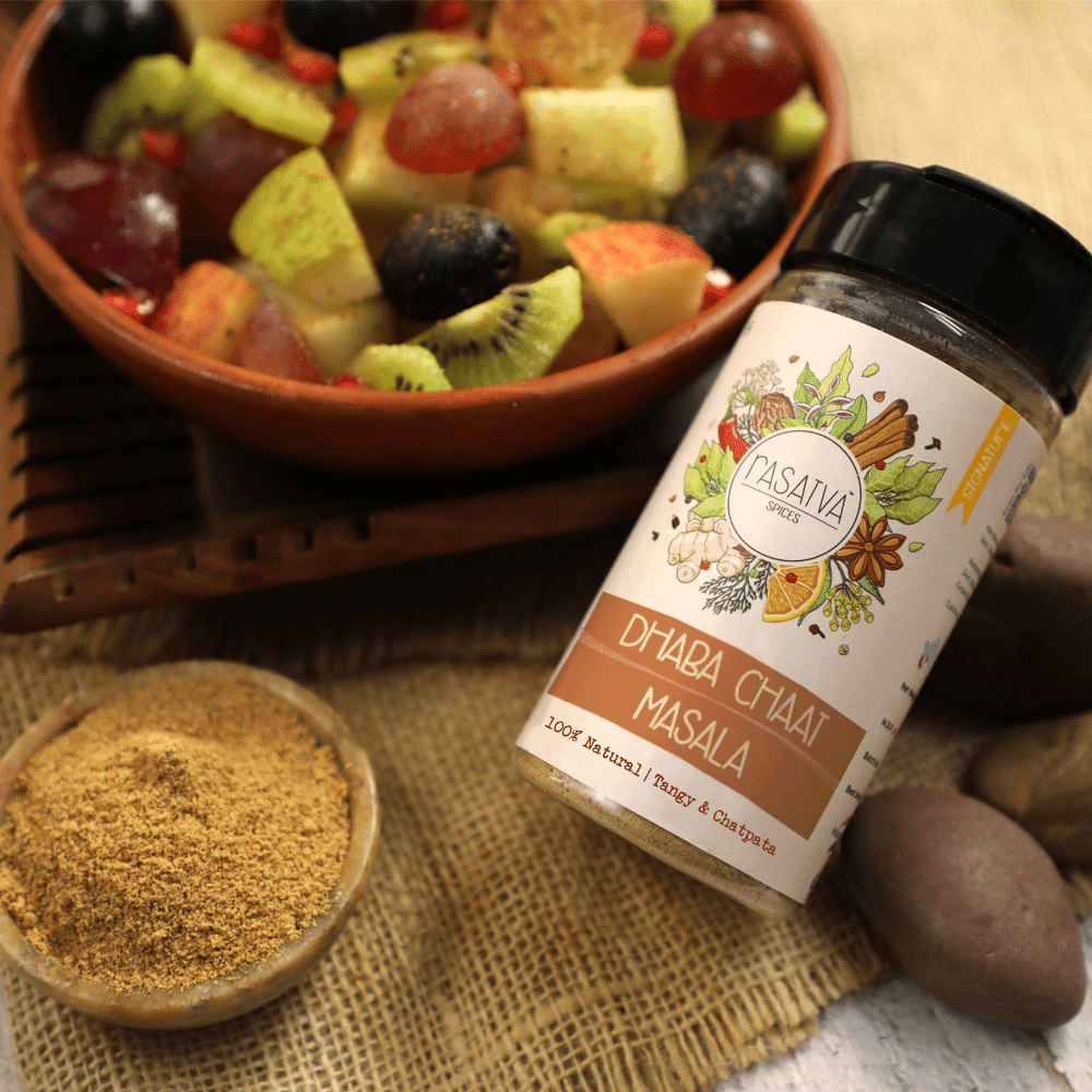 Dhaba Chaat Masala shown in a bottle and a bowl, with some of the spice sprinkled on fruits, highlighting its use as a flavorful seasoning.